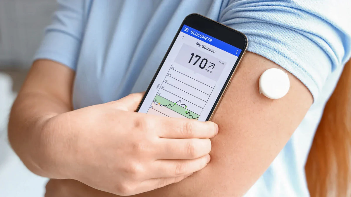 Persoon scant een glucosemeter op de bovenarm met een telefoon.