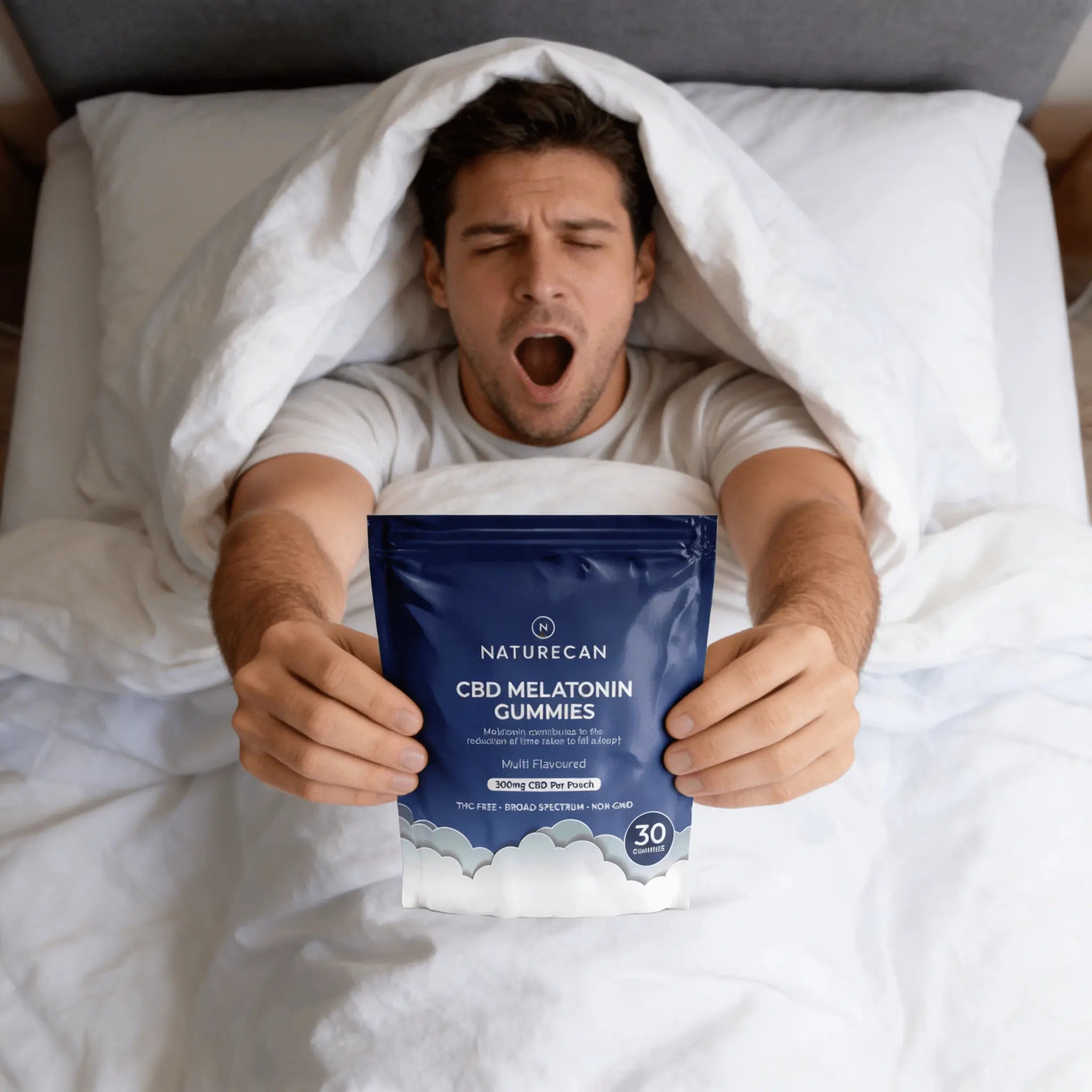 Man ligt in bed en houdt een zak Naturecan melatoninegummies vast.