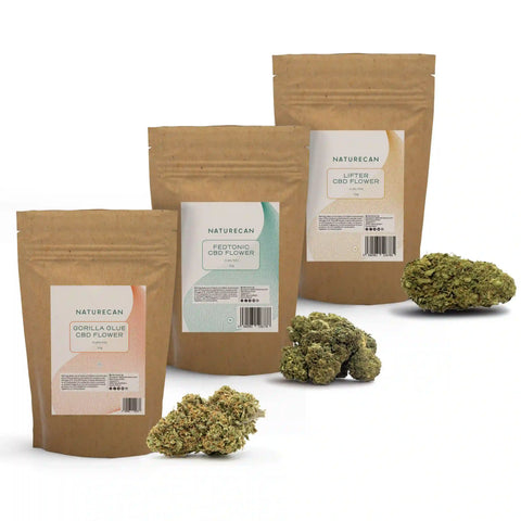 Drie bruine zakken CBD Bloemen - Ontspan Bundel, met labels zoals Gorilla Glue en Fedtonic, naast bloemen.